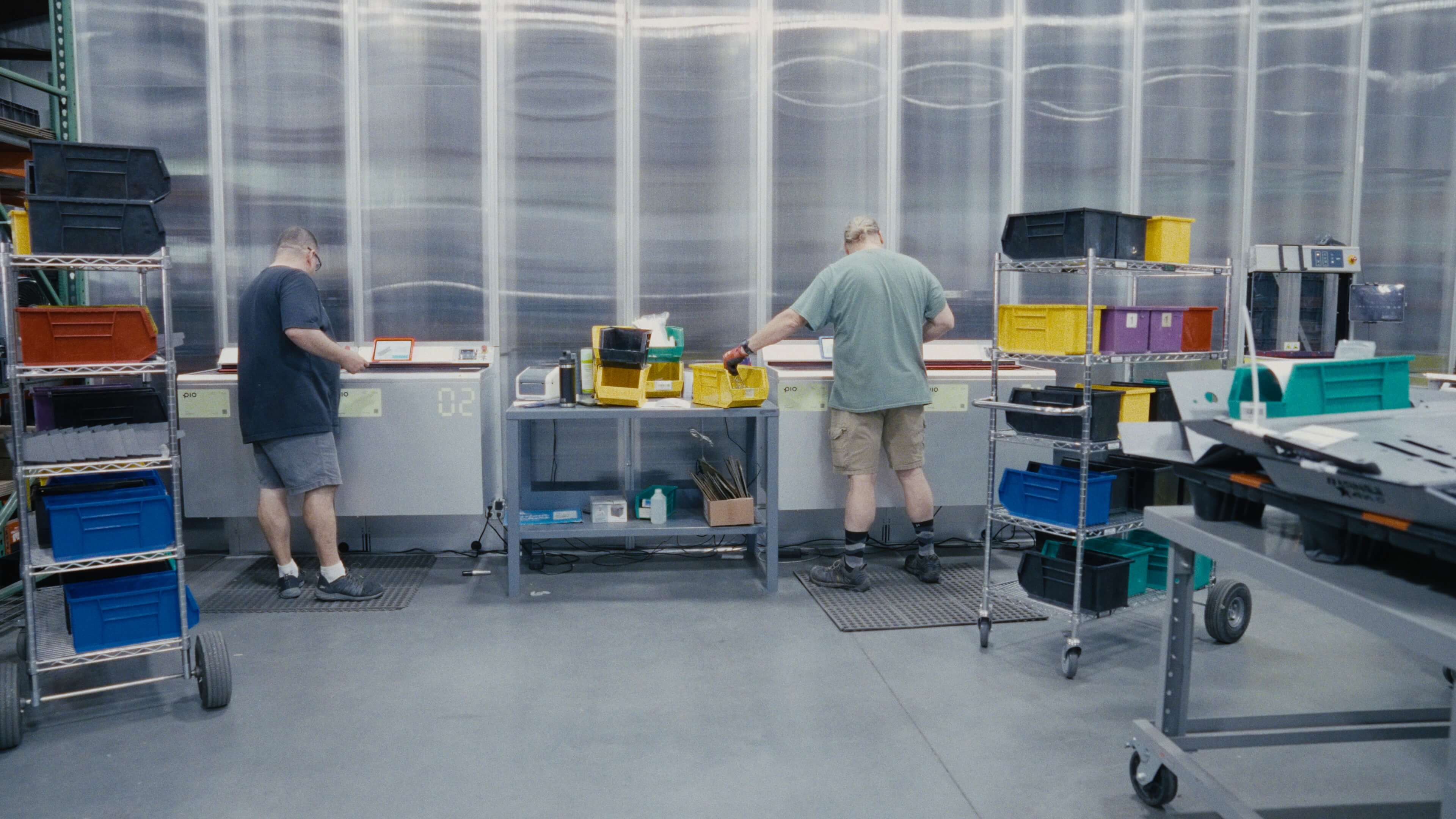 Two operators picking car parts at Pio ports in front of the cube storage grid, with bin carts beside them